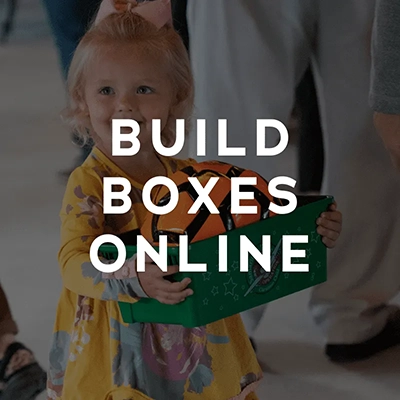 A square clickable image with the words 'build boxes onlilne' in a white and bold font over a photo of a girl holding an operation christmas child box 