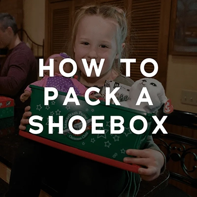 A square clickable image with the words 'how to pack a shoebox' in a white and bold font over a photo of a girl holding an operation christmas child box 