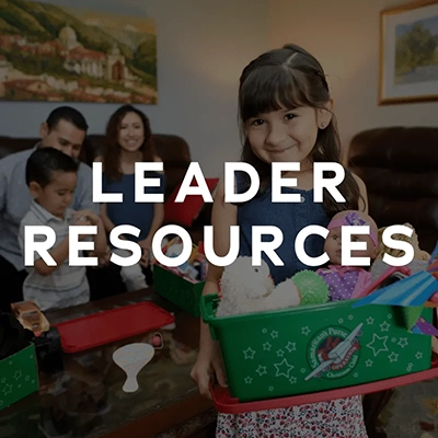 A square clickable image with the words 'leader resources' in a white and bold font over a photo of a girl holding an operation christmas child box 