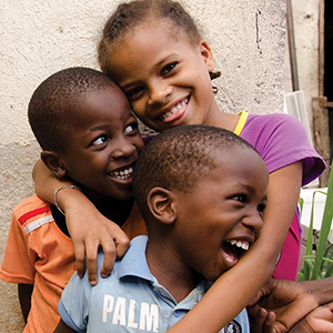 Three young kids smiling and hugging each other.